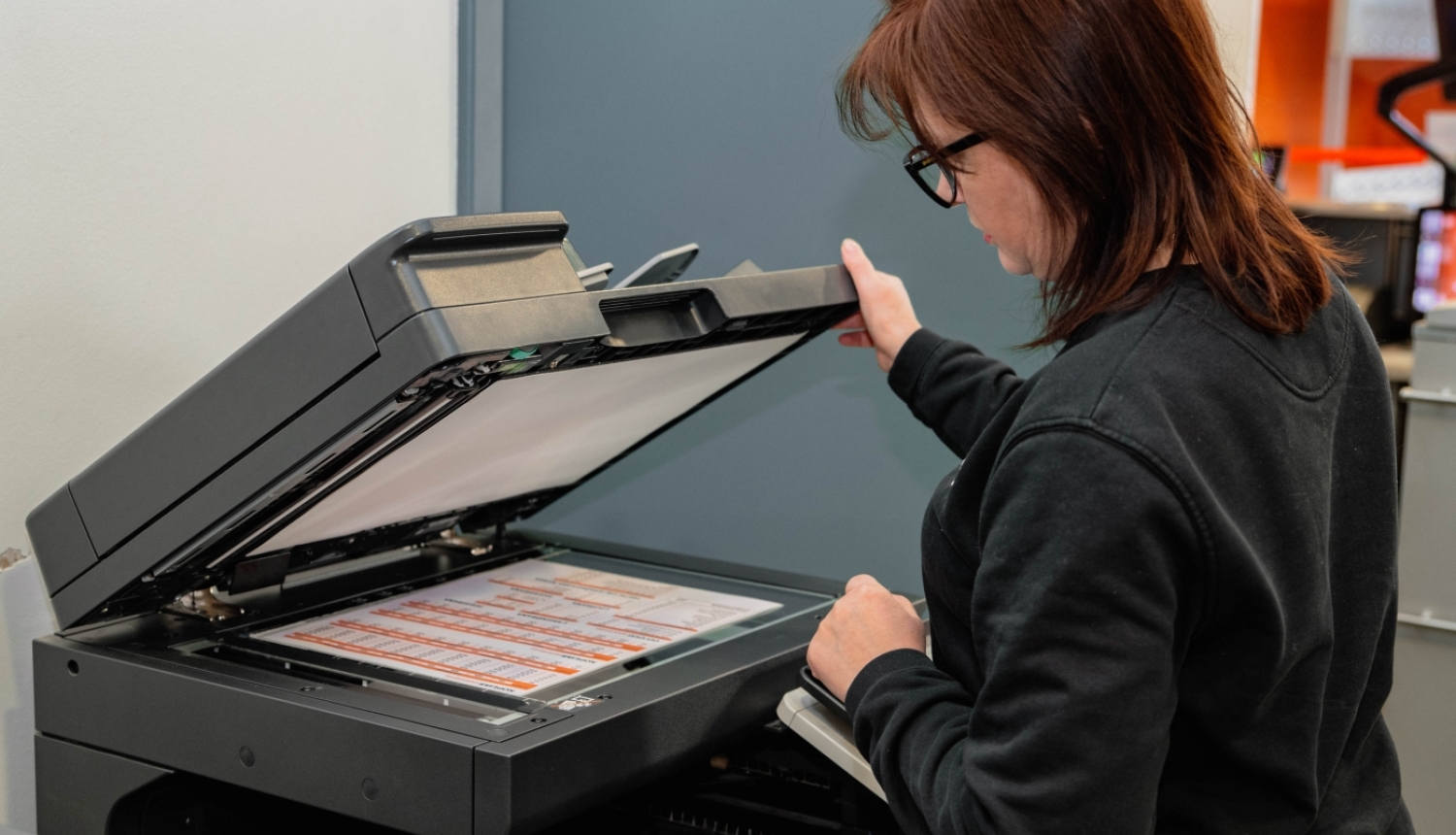 Sieviete, kas skenē dokumentus uz skenera, atverot tā vāku.