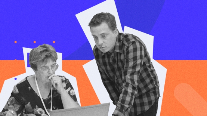 Vecāks cilvēks pie datora ar jaunāku cilvēku pāri plecam